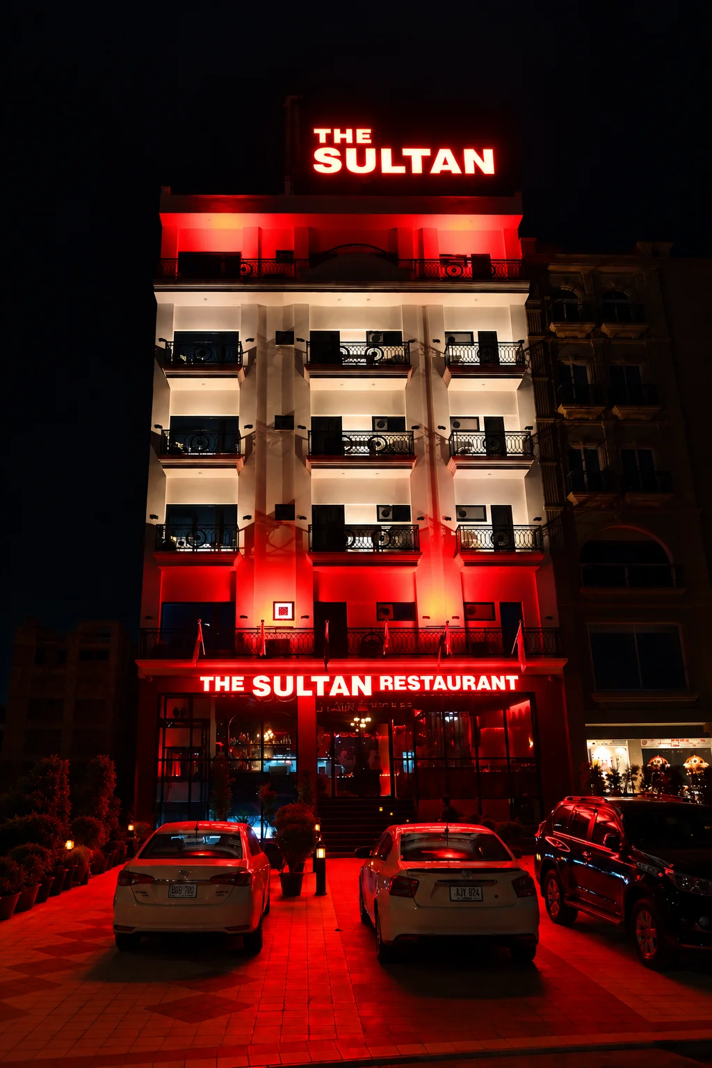 Exterior night view of The Sultan Hotel building featuring illuminated red neon signs for the hotel and restaurant near Islamabad Airport.